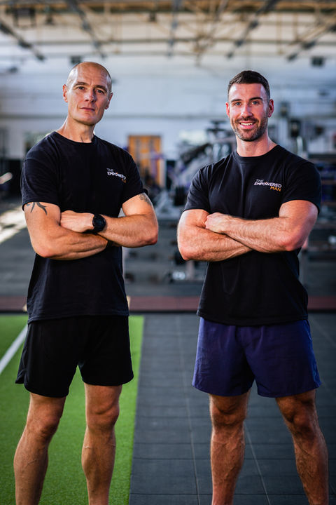 Two male models, showcasing The Empowered Man's online fitness coaching transformation program in a high-quality photo shoot by Jamie Bulman. The models are seen working out and flexing their muscles while wearing The Empowered Man apparel, promoting the 8-week transformation program. The photo shoot helped increase sales by 2000%.
