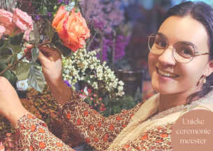 Vrouwelijke ceremoniemeester uit Tilburg met bloemenkrans, lachend bij kleurrijke rozen en bloemen. Unieke, persoonlijke aanpak voor stressvrije bruiloft in Brabant. Maison du Mariage.