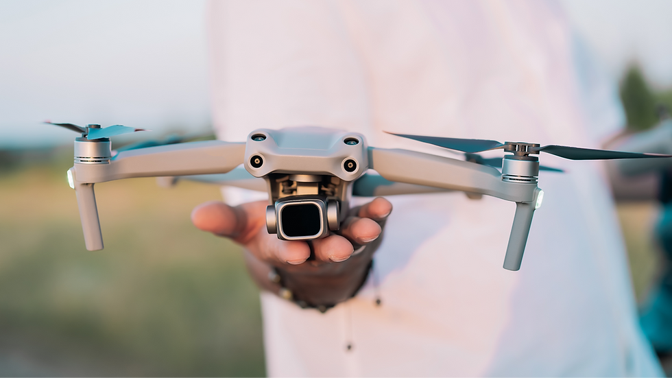A hand holds a gray drone in focus, set against a blurred outdoor background. The person wears a light shirt, exuding a calm, focused mood.