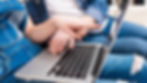 Two people in denim focus on a laptop. One points at the screen, and the other rests a hand on the keyboard. Casual and collaborative mood.