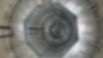 View of a large, industrial silo interior with a metallic spiral staircase. The setting is symmetrical, metallic gray, with geometric patterns.