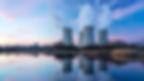 Nuclear power plant with four cooling towers emitting steam, reflected in a serene lake, under a vibrant pink and blue sunset sky.