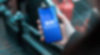Hand holding a smartphone displaying Tencent Music Entertainment logo on a blue screen. Background features a blurred staircase.
