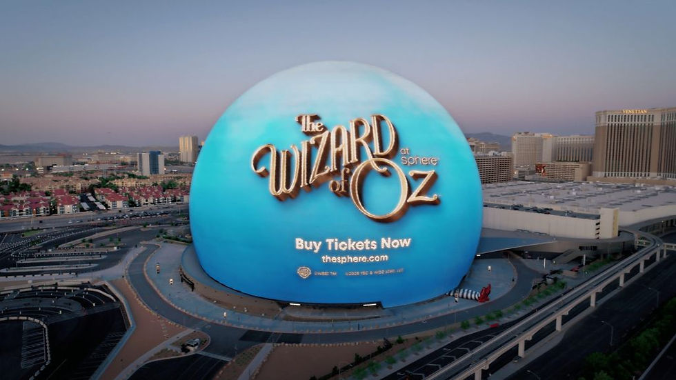 Blue dome displaying "The Wizard of Oz" text with "Buy Tickets Now" and URL. Urban backdrop with buildings under a clear sky at dusk.