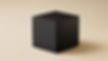 A black cube-shaped electronic device with USB ports sits on a beige surface. The simple, modern design contrasts with the plain background.