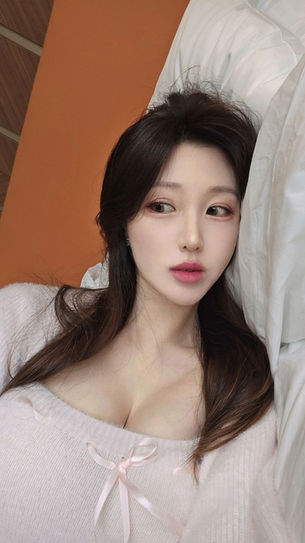 침대에 누워 핑크 니트 상의를 입은 Jennifer Vivian, 풍만한 가슴과 도발적인 표정이 매력적인 모습 – 아시안보지 단독 공개