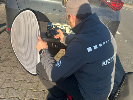 Car damage assessor taking photos of dented rear bumper in daylight