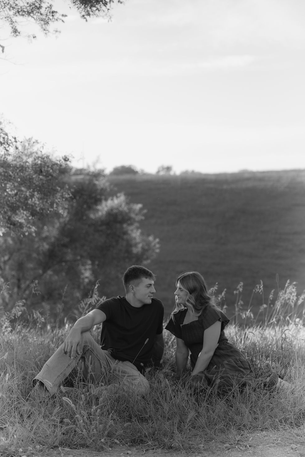 Black and white photo of a couple sitting together in tall grass, Sioux Falls couples photographer