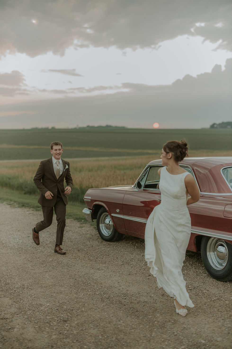 Groom running to his bride beside a vintage red car, Iowa wedding photographer