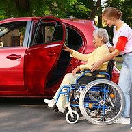 Young woman helping disabled grandmother in wheelchair to get into car outdoors.jpg