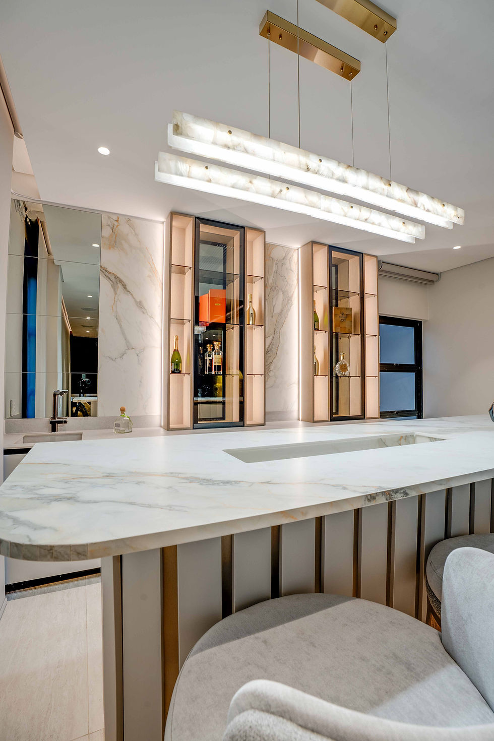 Contemporary gourmet kitchen with a central marble waterfall island, plush velvet bar stools, and a striking floor-to-ceiling glass display cabinet.