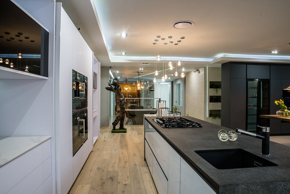 Modern kitchen with sleek black countertop, gas stove, and hanging lights. Statue in background, light wood floor, minimalistic decor.