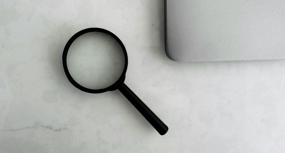 Minimalist flat lay of a black magnifying glass next to a silver laptop on a light grey surface - symbolising digital search or investigation.