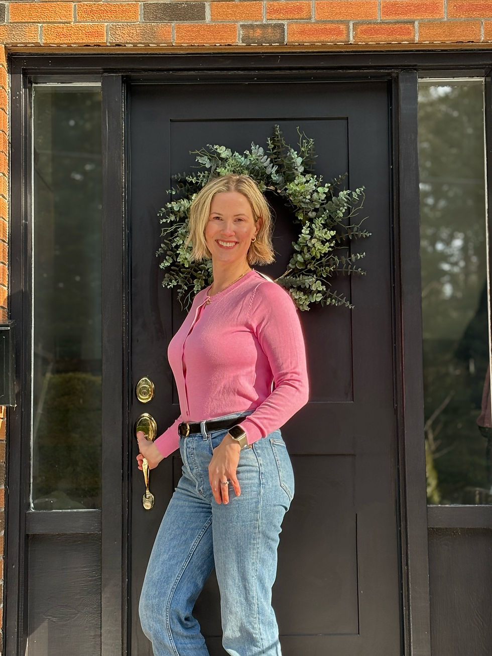 woman in pink cardigan and jeans standing by black front door