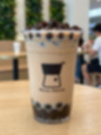 Light brown bubble tea with tapioca pearls in a plastic cup on a wooden table.