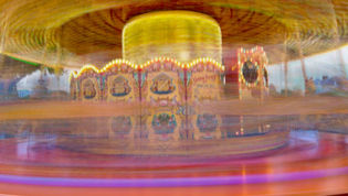 Blurred carousel, bright lights, and colourful decorations at a fairground.