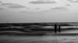 Silhouette of parent and child holding hands in the ocean water.