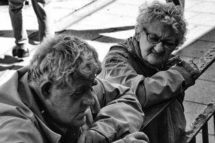 Elderly couple leaning on a railing, in a black and white photo. 