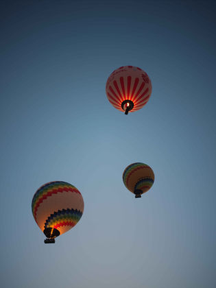 Three hot air balloons floating in a clear, blue evening sky.