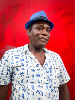Man in a blue hat and a white shirt with blue fish patterns stands against a vibrant red background.