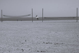 Volleyball nets on sandy beach with people and flag, seascape background.