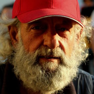 Older man wearing red cap looking at the camera with a white beard.
