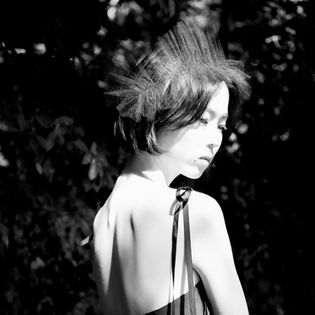 A profile of a woman with short hair and a decorative black tulle headpiece, captured in black and white.