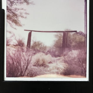 A Polaroid photo depicting a weathered gate set against a vast desert landscape.