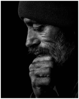 Close-up black and white portrait of a contemplative man in a beanie. He rests his chin on a hand, conveying deep thought and introspection.