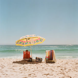 Beach scene with umbrella, chairs and towels, blue sky, sea. 
