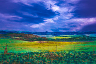 Green fields and dark sky landscape with fence and mountains in the background.