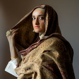 Woman in headscarf holding it, close-up portrait with sunlight and background.