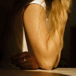 Woman's arm with gold ring, sunlit with long blonde hair, resting on surface.