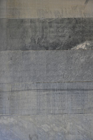 Gray textured concrete wall with horizontal lines. The surface has a rough, streaked pattern, conveying a rugged, industrial feel.