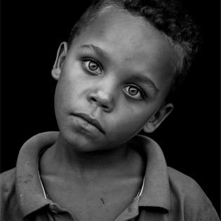 Close-up portrait of a young boy with dark eyes, looking at the camera.