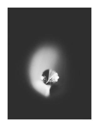 A monochrome abstract image features a single droplet in focus, surrounded by a blurred halo effect. The mood is mysterious and ethereal.