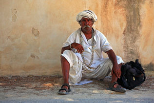 Man sitting on the ground, white outfit, turban, wall background.