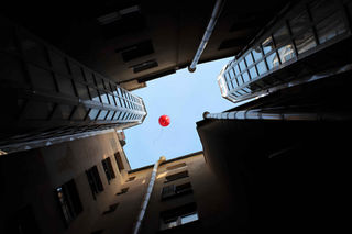 Looking up at a red balloon over several tall buildings in the sky.