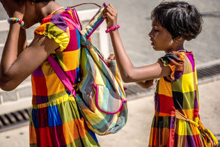 Two girls wearing colourful dresses with a backpack, and matching bracelets.