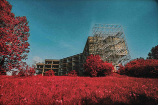 Building under construction with red grass and trees against a blue sky scenery.
