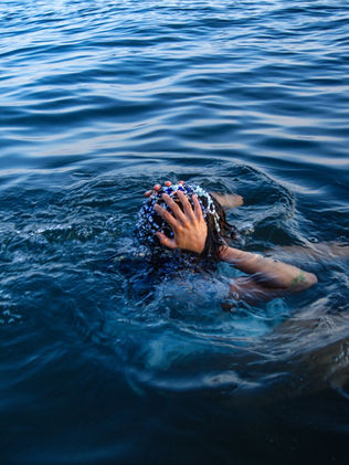 Person floating in clear blue water, hand covering head adorned. The scene exudes tranquility and connection with nature.