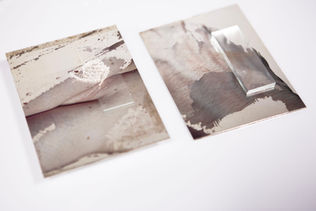 Two sheets of paper with abstract, marbled patterns in muted colors, one featuring a raised rectangular section.