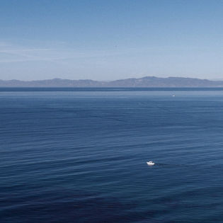 Small white boat floats on blue ocean under clear sky.