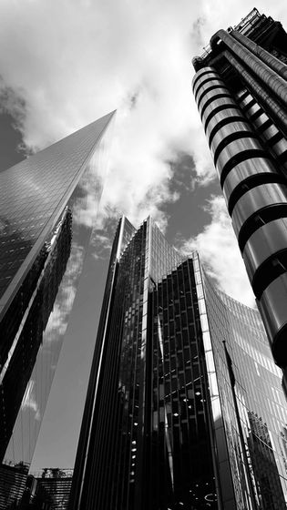 Low-angle view of modern buildings against a cloudy sky in black and white.