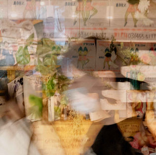 Blurred figures and objects in shop, with posters and shelves.