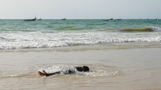 Person in water near beach with boats; ocean and clear sky background.