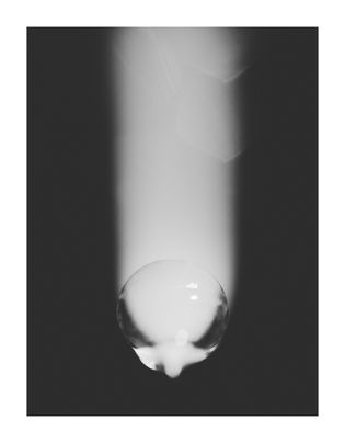 A single, glossy water droplet in grayscale, reflecting light, is centered against a blurred, dark background. The mood is calm and reflective.