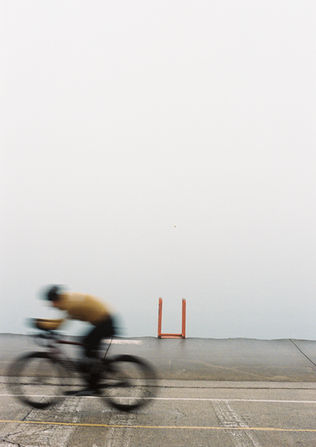 A blurred cyclist rides past a foggy waterfront with a red metal structure near the water's edge.