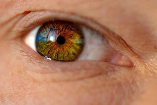 Close-up of a human eye with a vibrant green and brown iris, reflecting light. The intricate patterns and textures create a vivid, striking effect.