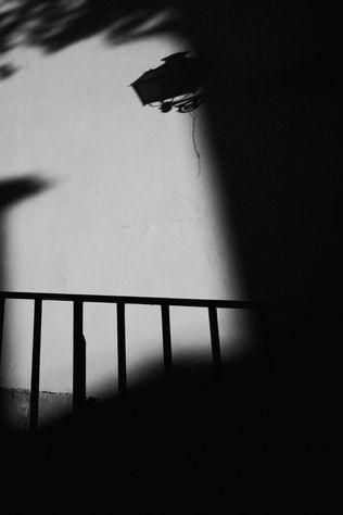A shadow of a lamp post cast on a wall, with part of a railing visible in the foreground.